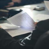 机で複数の資料を読み比べ、判断を見直す人物