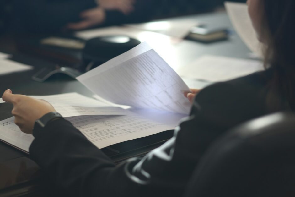 机で複数の資料を読み比べ、判断を見直す人物
