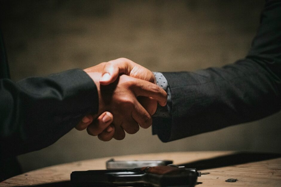 木製テーブルを挟んで二人が握手する様子。信頼と誠実な約束を象徴するイメージ