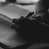 ノートにペンで書き込む手元。年齢を重ねても続く学びと日々の記録を象徴する写真